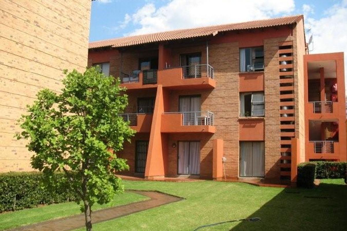 A view of the rear apartment building facade featuring brick construction, multiple balconies with metal railings, and a well-maintained communal garden area.