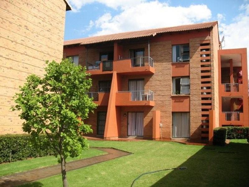 A view of the rear apartment building facade featuring brick construction, multiple balconies with metal railings, and a well-maintained communal garden area.
