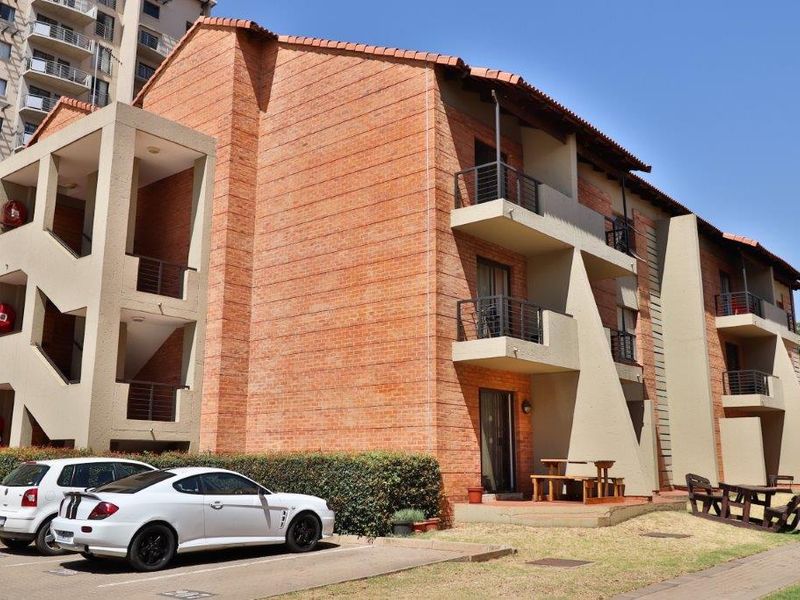 A multi-story apartment building featuring exposed brick exterior, private balconies with metal railings, and a paved ground-level patio area.
