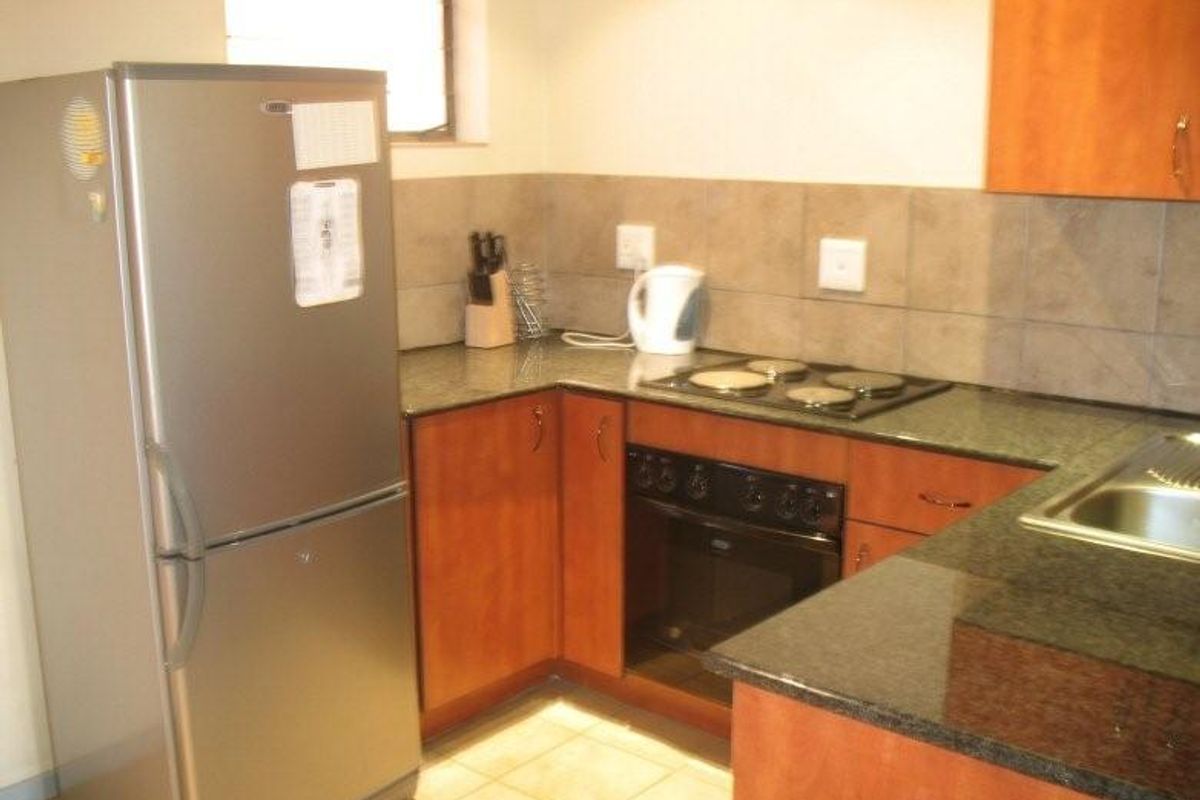 A functional kitchen featuring wood-finish cabinetry, granite countertops, a built-in oven, electric hob, and tiled backsplash.