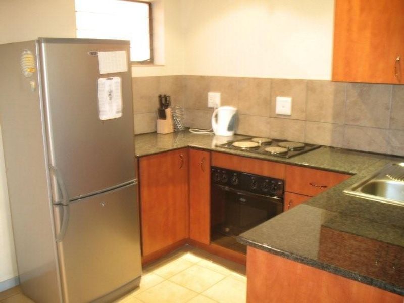 A functional kitchen featuring wood-finish cabinetry, granite countertops, a built-in oven, electric hob, and tiled backsplash.