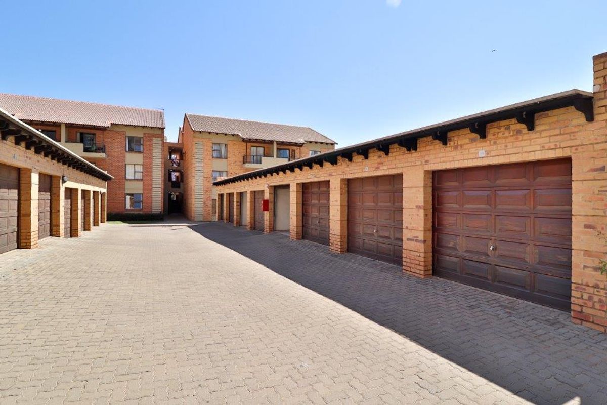 A view of a residential apartment complex featuring a row of individual brick garages with sectional doors and a paved driveway.