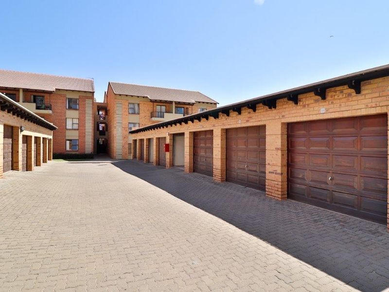 A view of a residential apartment complex featuring a row of individual brick garages with sectional doors and a paved driveway.