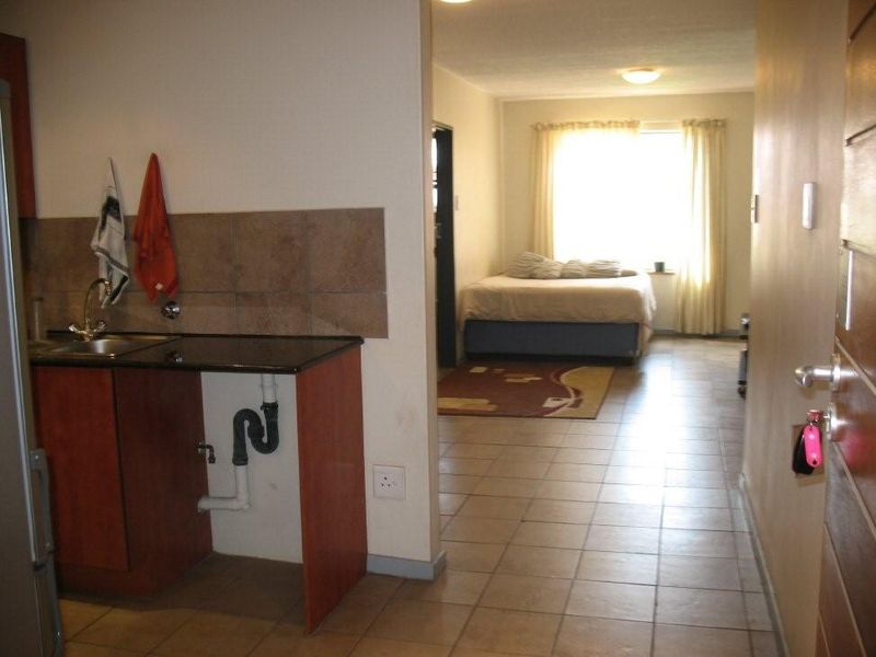 Open plan apartment layout featuring a kitchenette with granite countertops and tiled flooring, leading into a bedroom area.