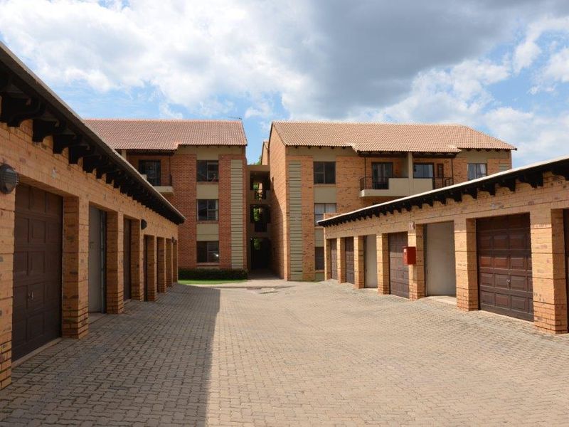Exterior view of an apartment complex featuring face brick buildings, a paved driveway, and a row of individual garage units.