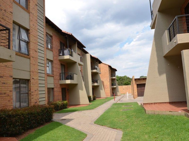 Exterior view of a multi-story apartment complex featuring face brick facades, private balconies, and a well-maintained paved walkway through a landscaped garden area.