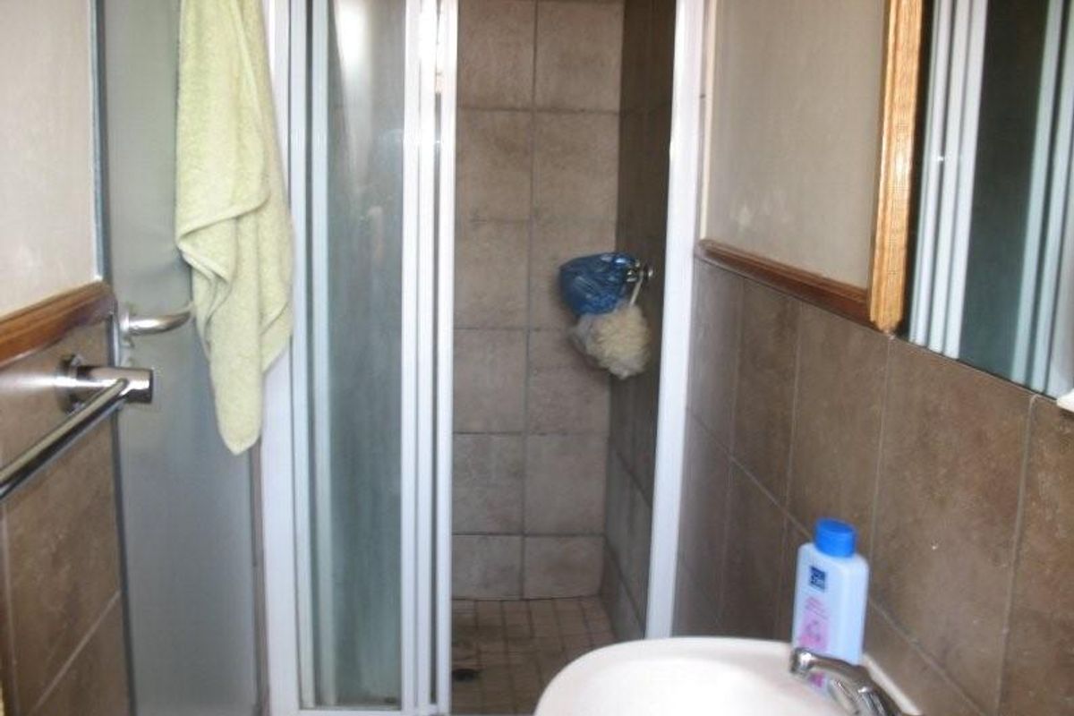 A compact bathroom featuring a shower enclosure with tiled walls and a basin with a chrome faucet.