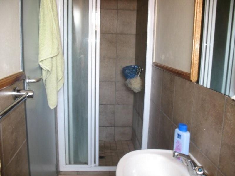 A compact bathroom featuring a shower enclosure with tiled walls and a basin with a chrome faucet.