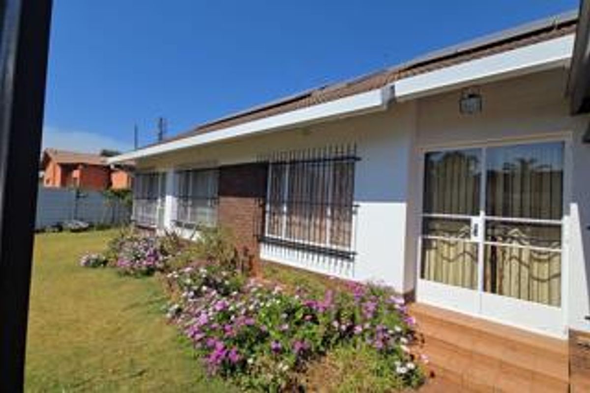 Rear exterior view of the house featuring a tiled patio, sliding glass doors, security bars on windows, and a well-maintained garden area.