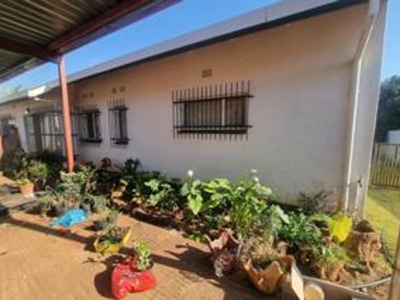 Rear exterior view of the house featuring a covered patio area, security bars on windows, and established garden beds along the building perimeter.