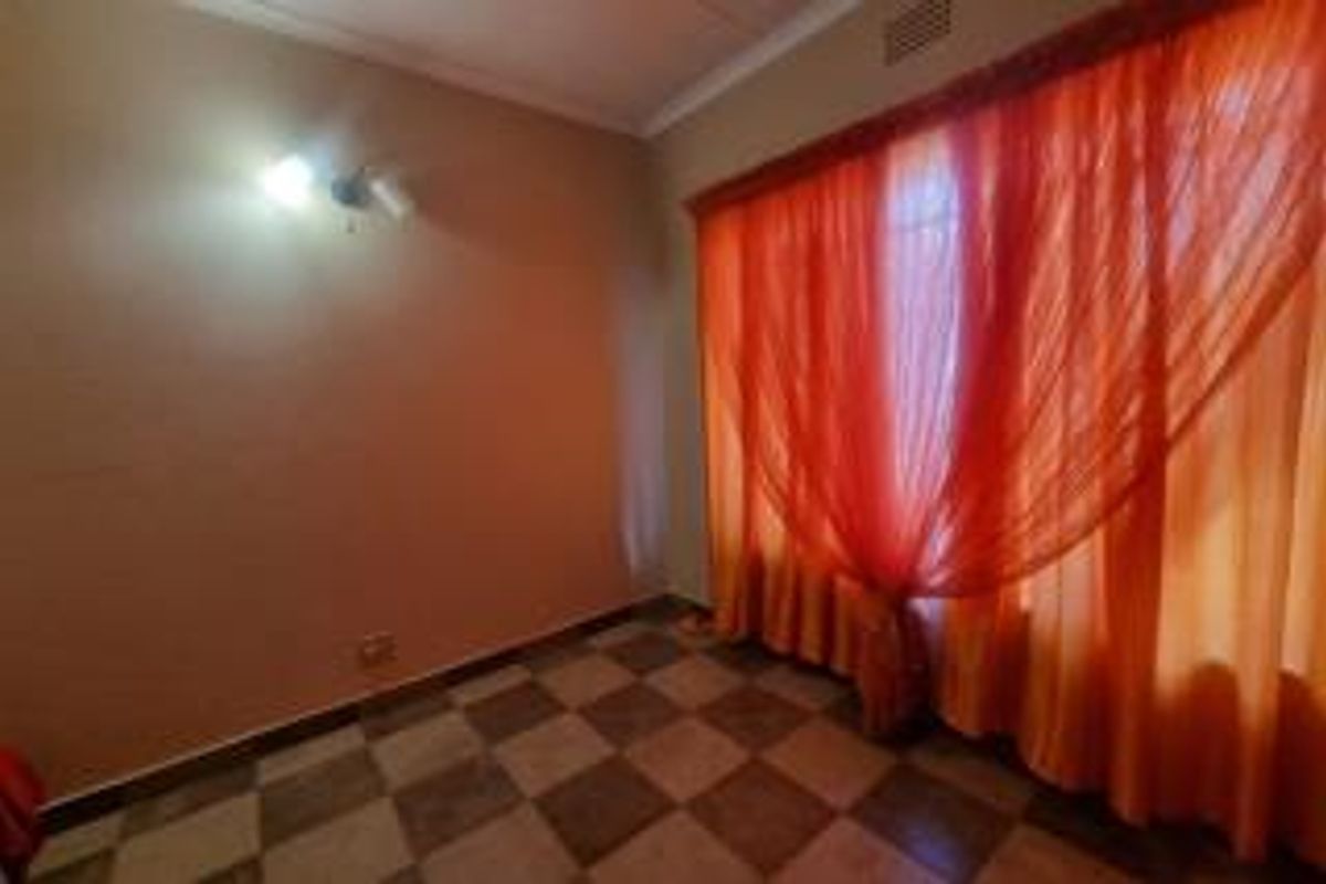 An empty bedroom featuring tiled flooring, a wall-mounted light fixture, and large windows covered by curtains.