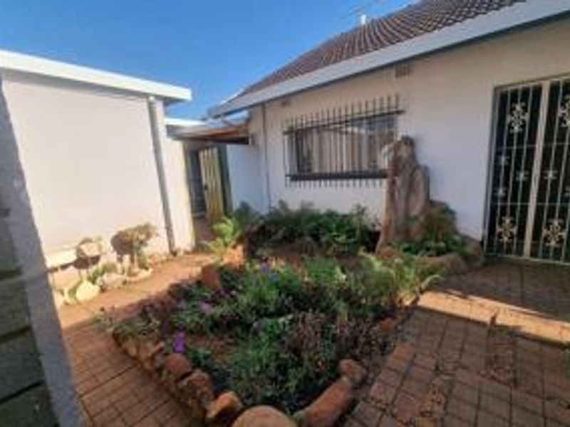 A rear courtyard area featuring paved flooring, a small garden bed, and security bars on the windows and doors.