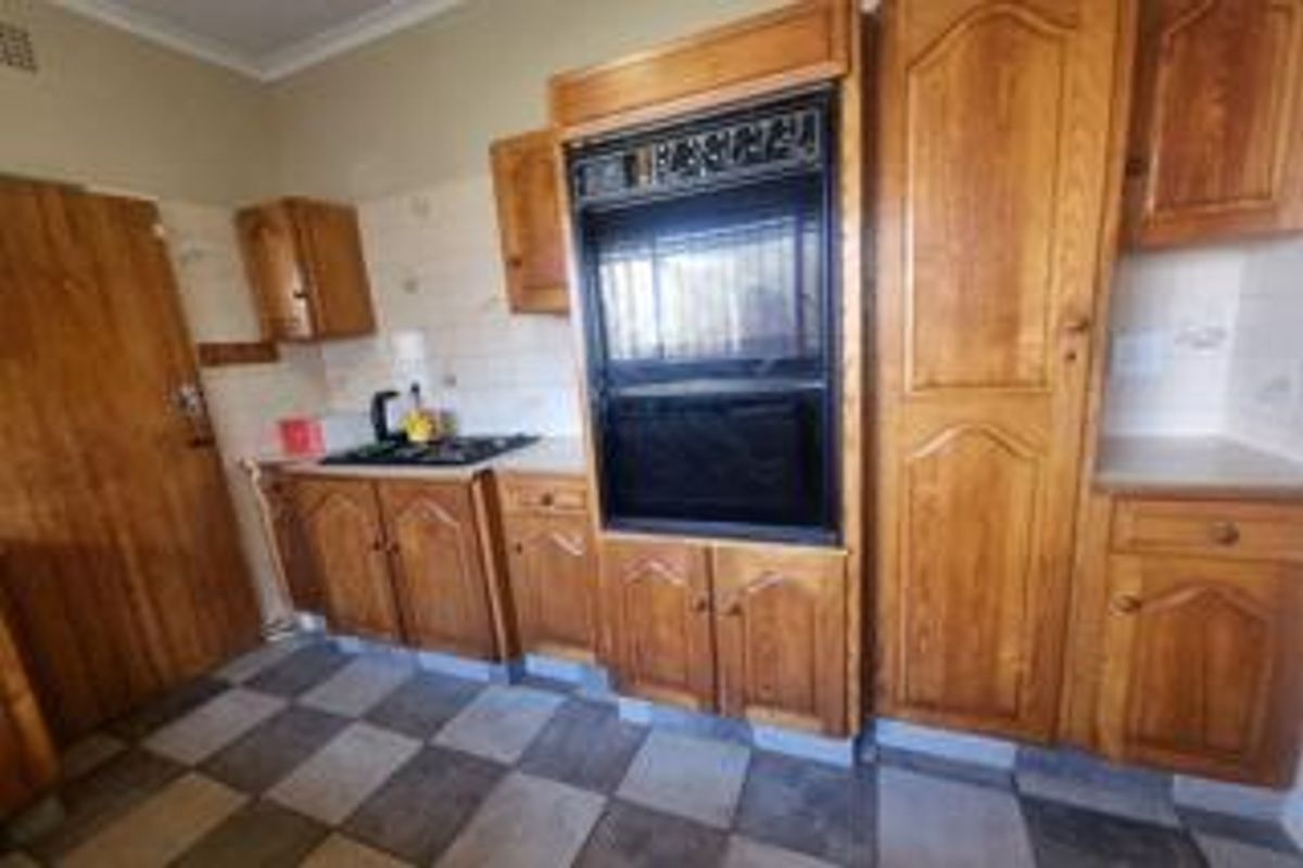 A dated kitchen featuring traditional wooden cabinetry, a built-in oven, gas hob, and checkered tiled flooring.