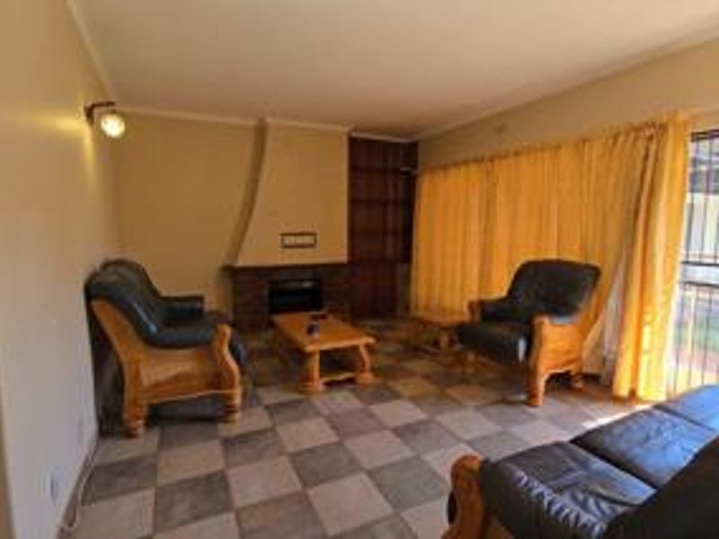 A living room featuring a brick fireplace, built-in shelving, and tiled flooring, with access to an outdoor area through a security gate.