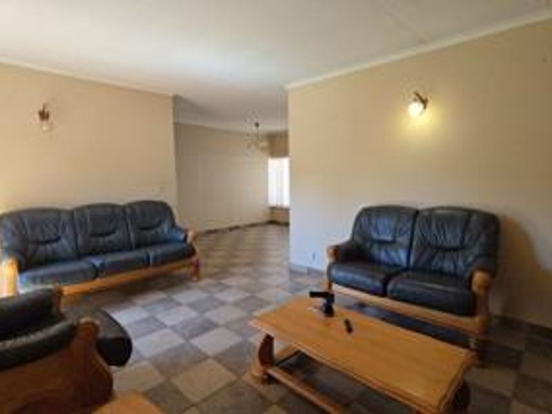 A spacious living room featuring tiled flooring, coved ceilings, and wall-mounted lighting, offering a neutral base for potential interior updates.