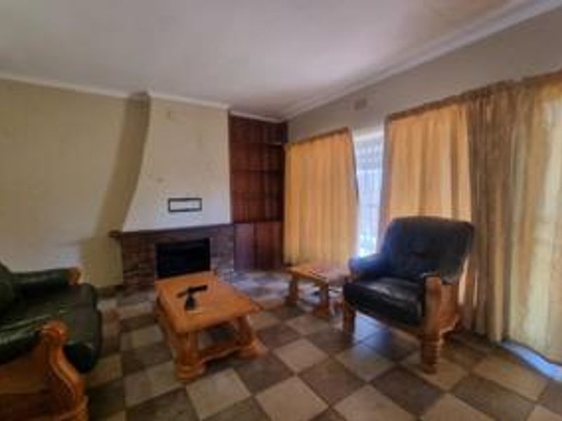Living room featuring a brick fireplace, built-in wooden shelving, and tiled flooring, offering a dated interior space with potential for modernization.