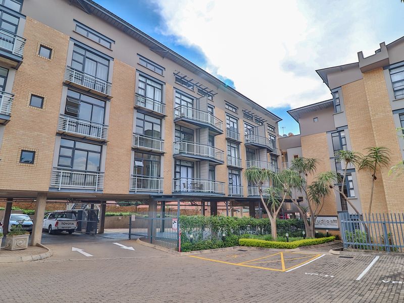 Exterior view of a modern multi-story apartment complex featuring brick facades, private balconies, and a paved driveway with covered parking.