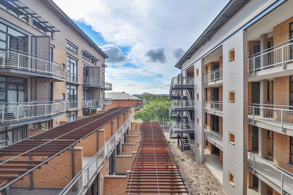 View of the apartment complex exterior featuring brick facades, metal staircases, balconies, and a central timber pergola walkway.