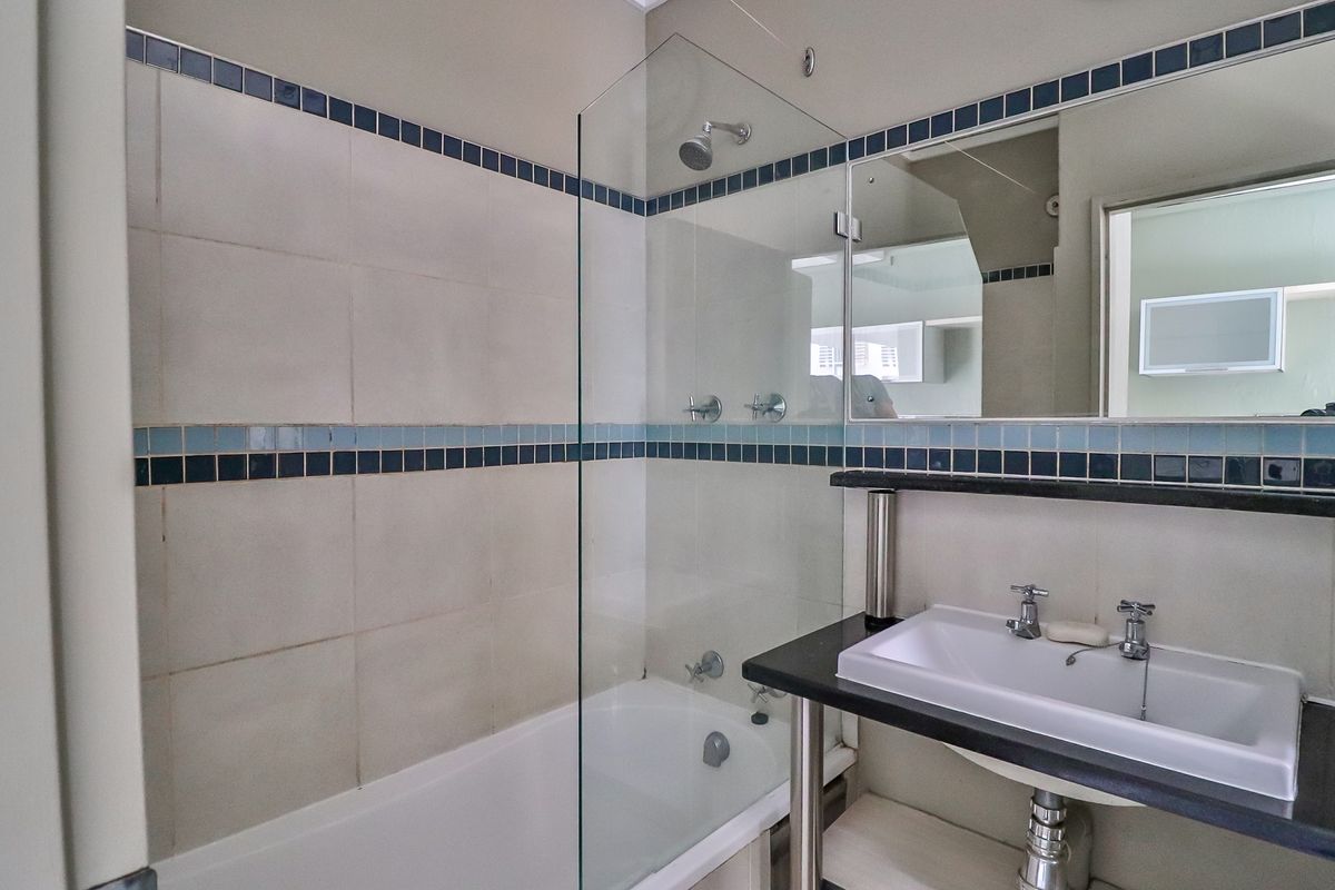 A functional bathroom featuring a bathtub with a glass shower screen, a wall-mounted basin with a granite vanity top, and classic tiled walls.