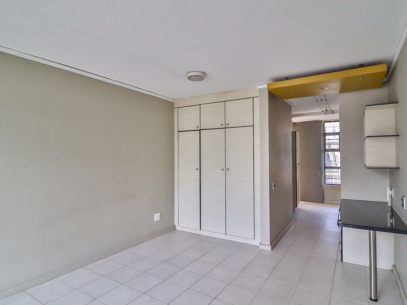 An open-plan living area featuring neutral tiled flooring, built-in storage cupboards, and a breakfast counter with floating shelving.