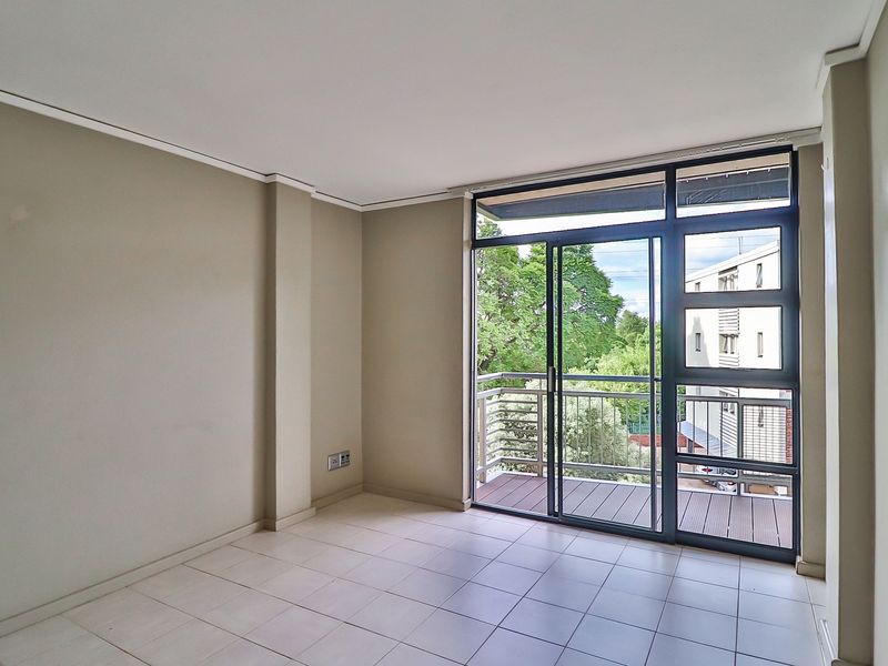 A bright, empty living area featuring neutral tiled flooring, coving, and a large sliding glass door providing direct access to a private balcony.