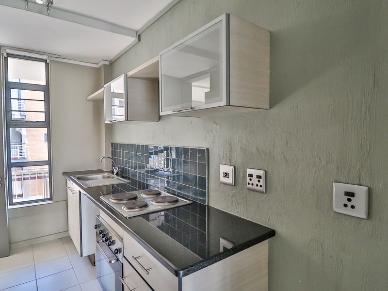 A compact, functional kitchen featuring built-in cabinetry, a granite countertop, an electric hob, and an integrated oven with a tiled backsplash.