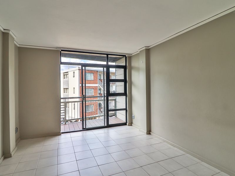 A bright, empty living room featuring neutral tiled flooring and a large sliding glass door providing access to a private balcony.