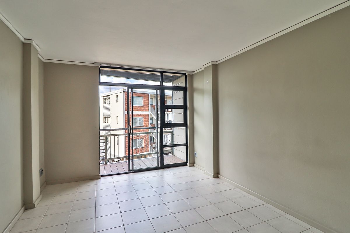 A bright, empty living room featuring neutral tiled flooring and a large sliding glass door providing access to a private balcony.