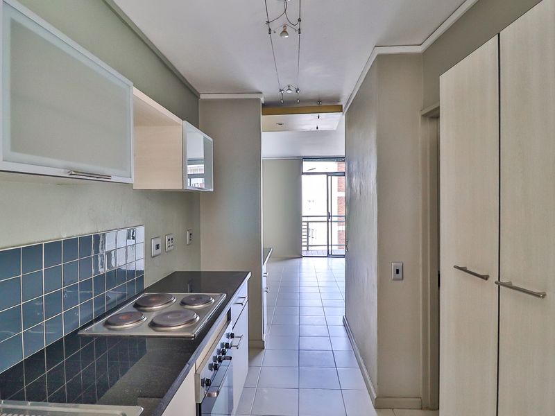 A clean, functional kitchen featuring built-in cabinetry, a stone countertop, an electric hob, and an integrated oven, leading into an open-plan living area.