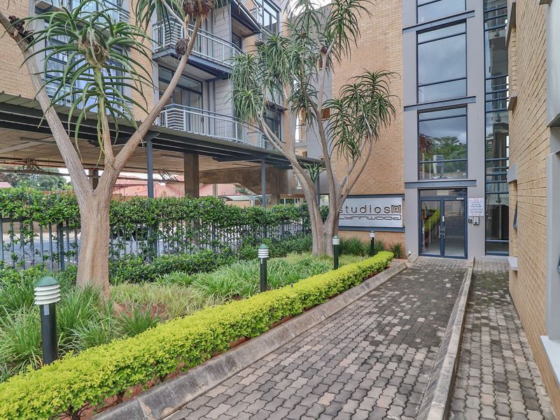 The front entrance of the apartment complex features a paved walkway, landscaped garden, and modern brick and glass facade.