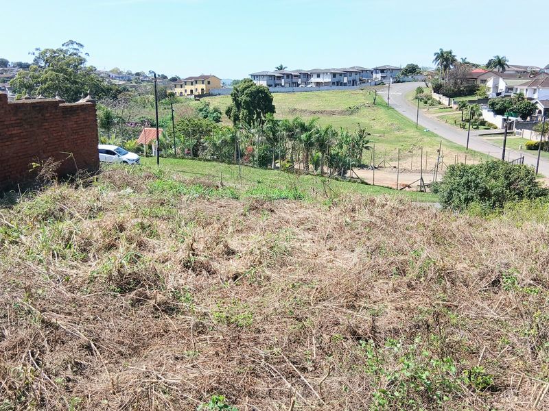 A vacant residential plot featuring a brick boundary wall and views of the surrounding neighborhood and street.