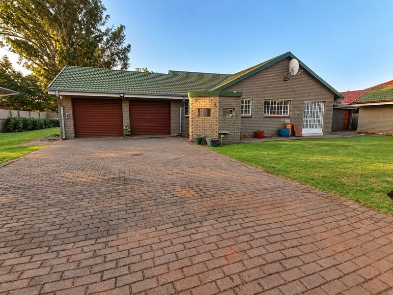 Front view of a brick house featuring a double garage, paved driveway, and a well-maintained lawn.