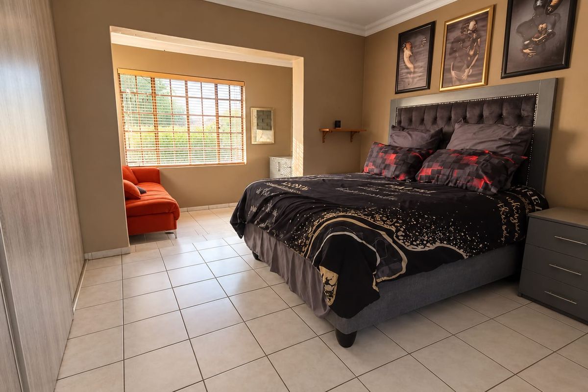 Spacious bedroom featuring tiled flooring, built-in cupboards, and a recessed window area with venetian blinds, offering a comfortable and functional living space.