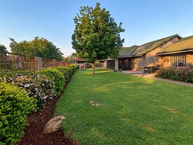 Spacious rear garden featuring a well-maintained lawn, established trees, paved patio area, and secure perimeter fencing adjacent to the brick-built house.