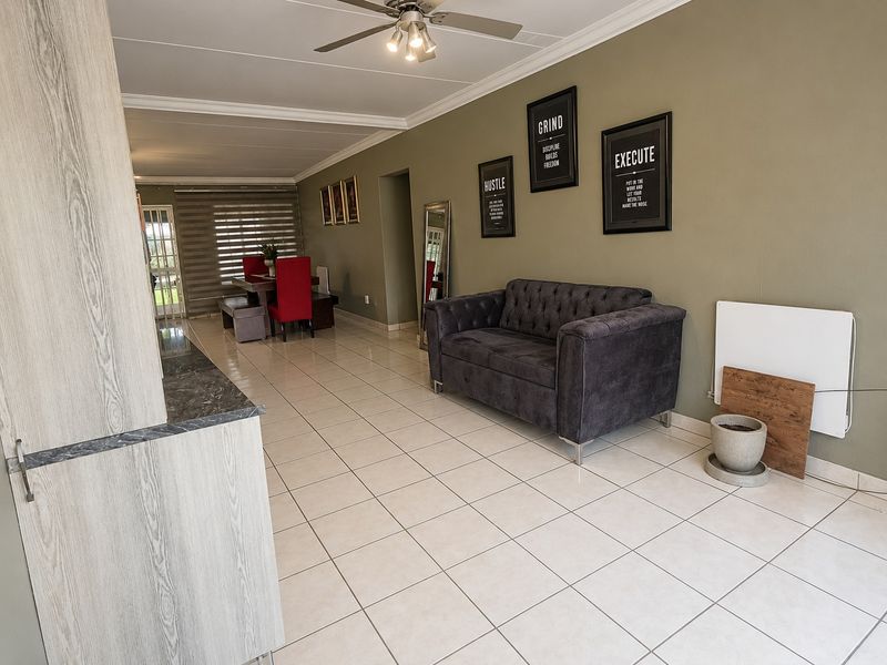 Spacious open-plan living and dining area featuring neutral tiled flooring, a ceiling fan, and a modern kitchen corner with stone countertops.