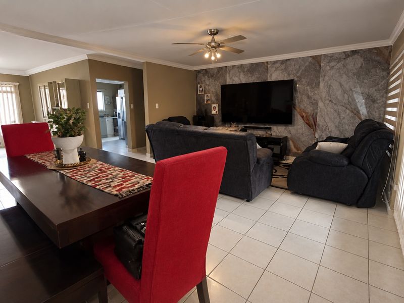 Spacious open-plan living and dining area featuring tiled flooring, a decorative feature wall, and a ceiling fan, with an adjacent kitchen view.