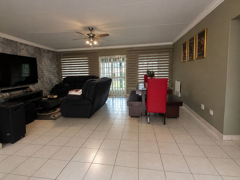 Spacious open-plan living and dining area featuring tiled flooring, a marble-look feature wall, ceiling fan, and direct access to the exterior via a security gate.