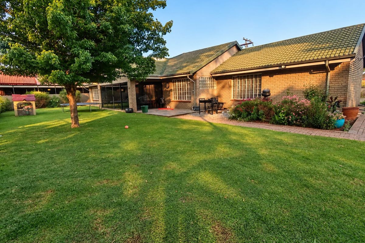 Rear view of the property featuring a brick facade, tiled roof, and a paved patio area overlooking a well-maintained garden.