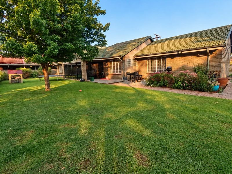 Rear view of the property featuring a brick facade, tiled roof, and a paved patio area overlooking a well-maintained garden.