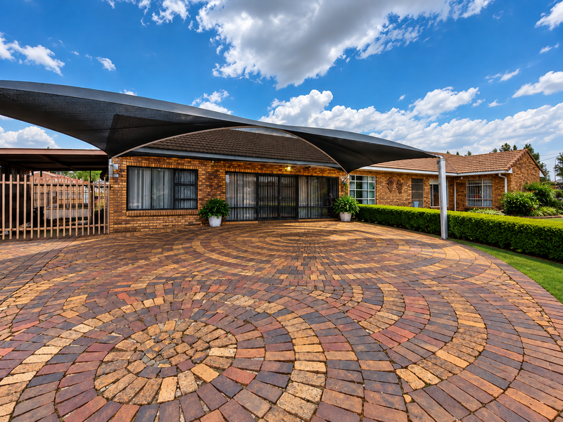 A well-maintained front exterior featuring a circular brick paved driveway, a large shade sail, and a classic face brick facade with secure metal gates.