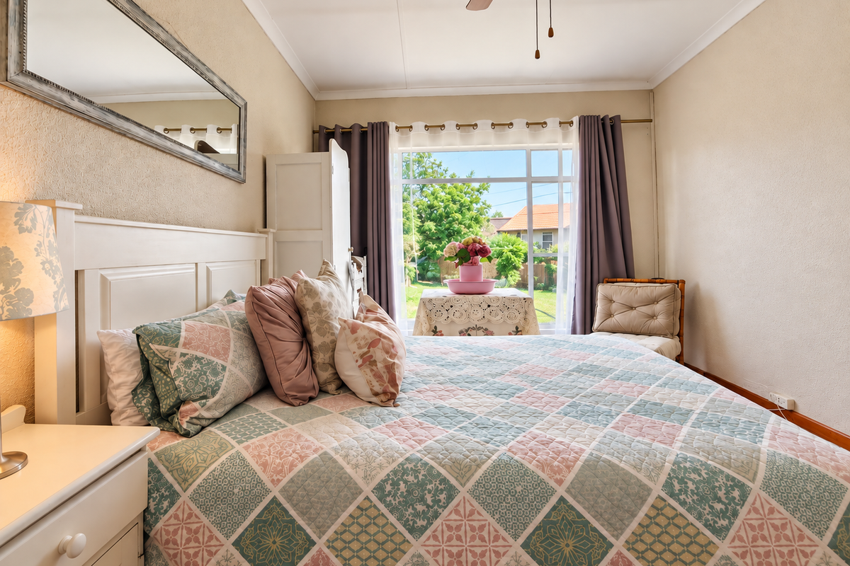 A well-maintained bedroom featuring a ceiling fan, neutral wall finishes, and a large window providing natural light and garden views.