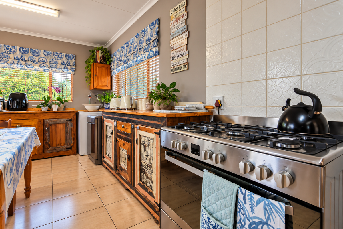 A functional kitchen featuring a stainless steel gas stove, tiled backsplash, and rustic wooden cabinetry with ceramic floor tiles.