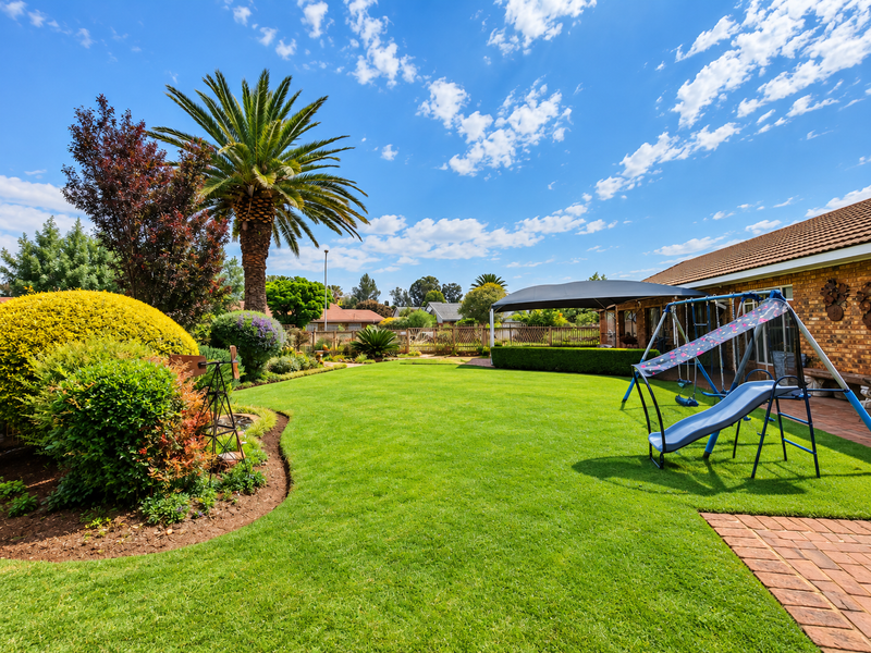 A well-maintained rear garden featuring a lush green lawn, mature palm tree, and brick-paved patio area adjacent to the house.