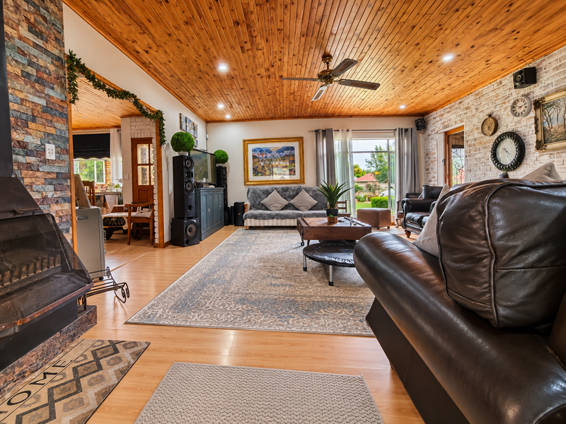 Spacious living room featuring a warm timber ceiling, stone-clad fireplace, and exposed brick wall, with direct access to the outdoor area.