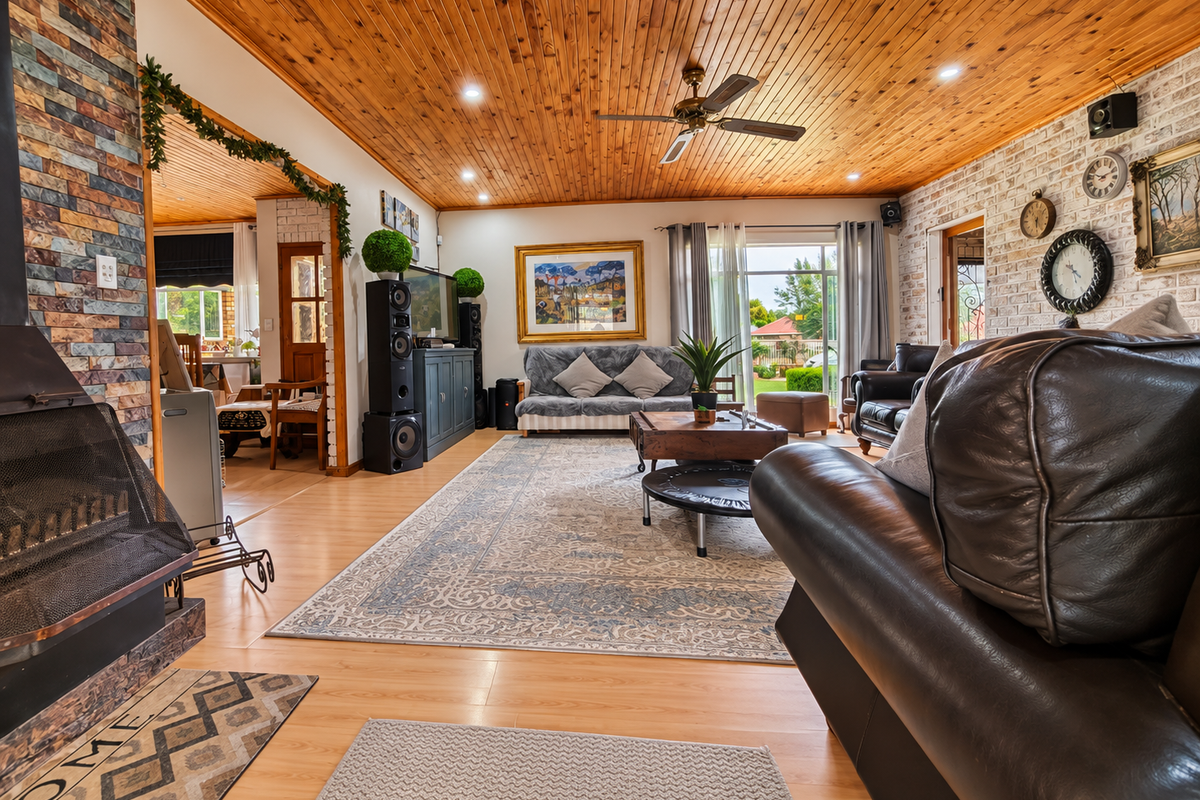 Spacious living room featuring a warm timber ceiling, stone-clad fireplace, and exposed brick wall, with direct access to the outdoor area.