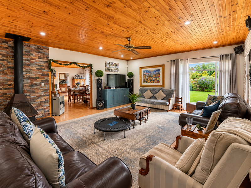 Spacious living room featuring a warm timber-clad ceiling, a stone-clad fireplace, and large sliding glass doors providing direct access to the garden.