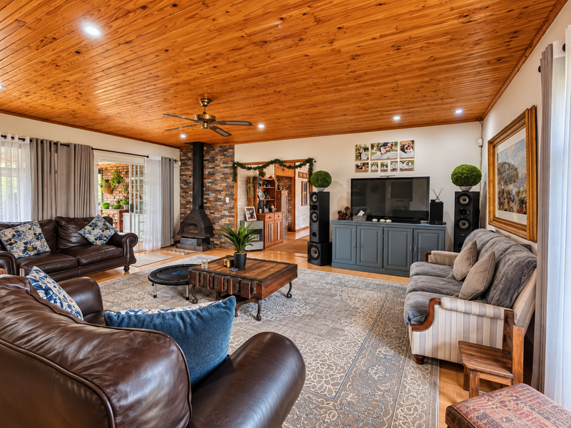 Spacious living room featuring a warm timber-clad ceiling, a prominent stone-clad fireplace, and recessed lighting, creating a cozy and inviting atmosphere.