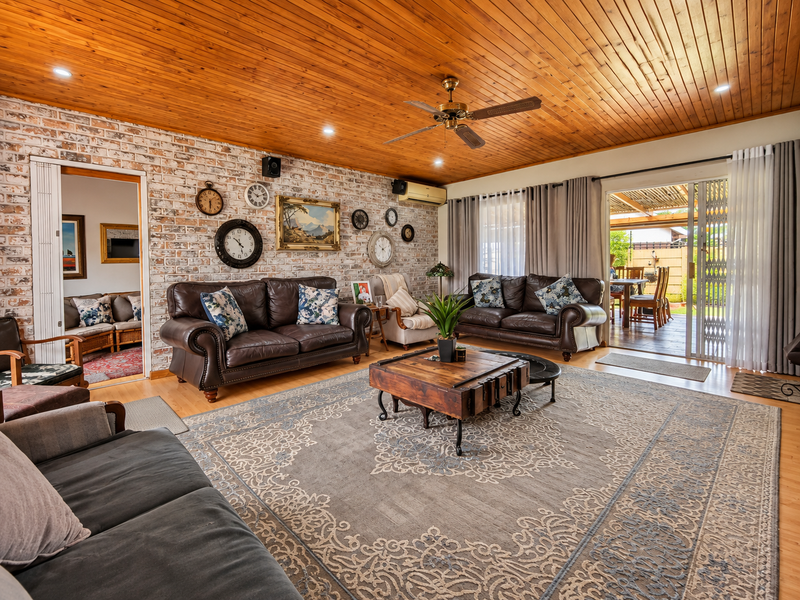 Spacious living room featuring a distinctive timber ceiling, exposed brick feature wall, and large sliding doors providing seamless access to the outdoor patio area.