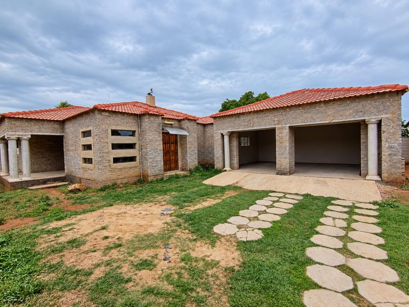 Front view of a stone-clad house featuring a double garage, terracotta roof tiles, and a stone-columned entrance with an unfinished garden area.