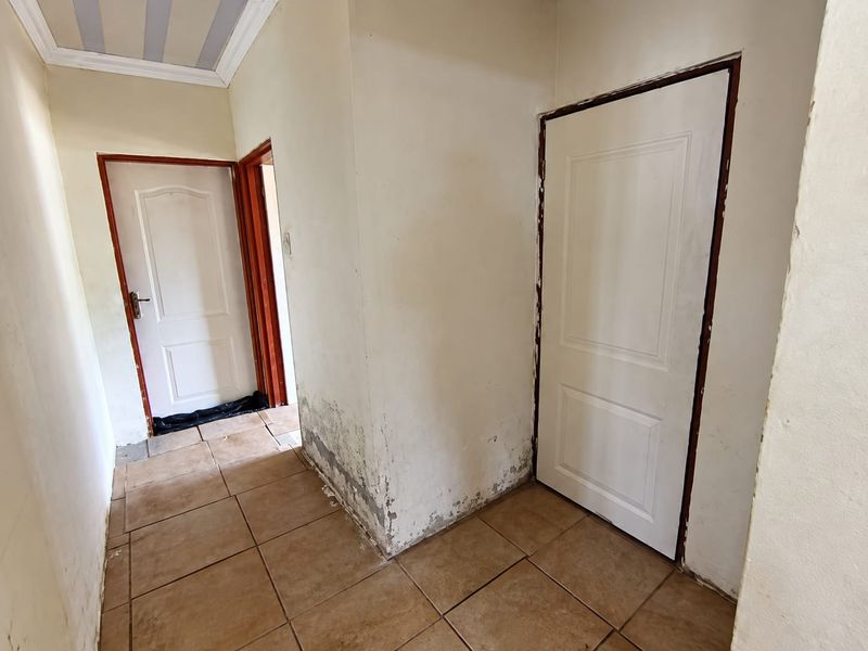 A hallway featuring tiled flooring and multiple internal doors, showing visible signs of wall damage and peeling paint requiring maintenance.
